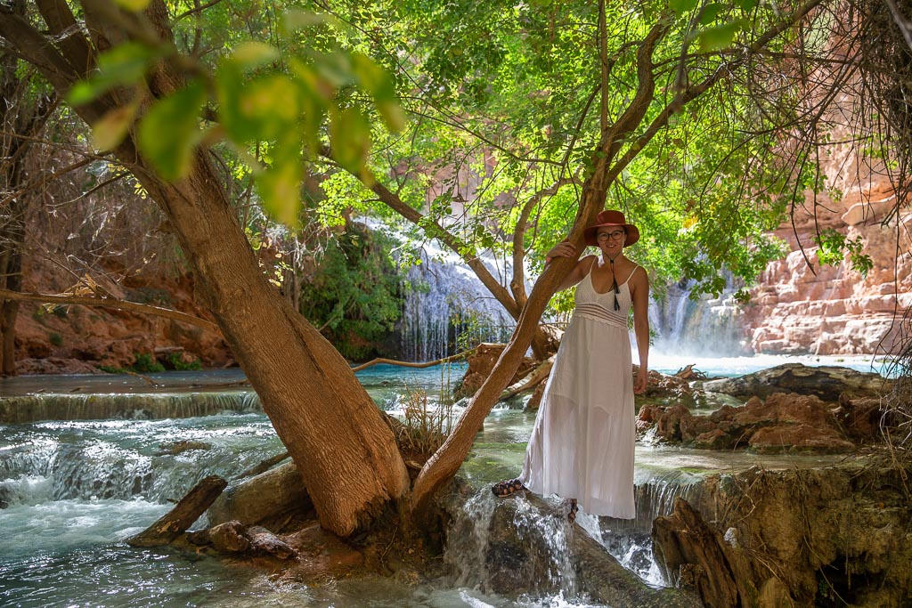 Agnes Stabinska, an author, in a long white dress next to tree and Beaver Falls at Havasupai. 