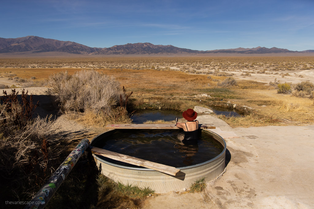 Agnes Stabinska, the author, in black swimsuit and red hat is relax in spencer hot springs in nevada. It is immersed in a round, small pool and overlooks the desert hills of Nevada.