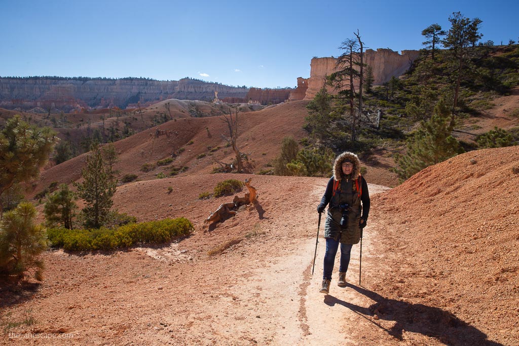 Agnes Stabinska, the author, hiking in Bryce Canyon National Park. She has warm jacket and trekking poles, at the backdrop are oranges hoodoos.