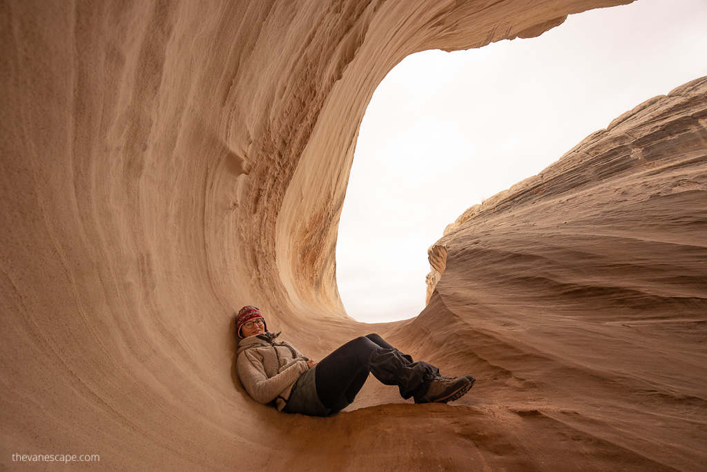 Agnes Stabinska, the author and co-owner of The Van Escape blog, sits against a slightly orange wall reminiscent of the trough of the Nautilus Formation in Utah. He is wearing a warm hat and a warm fleece jacket.