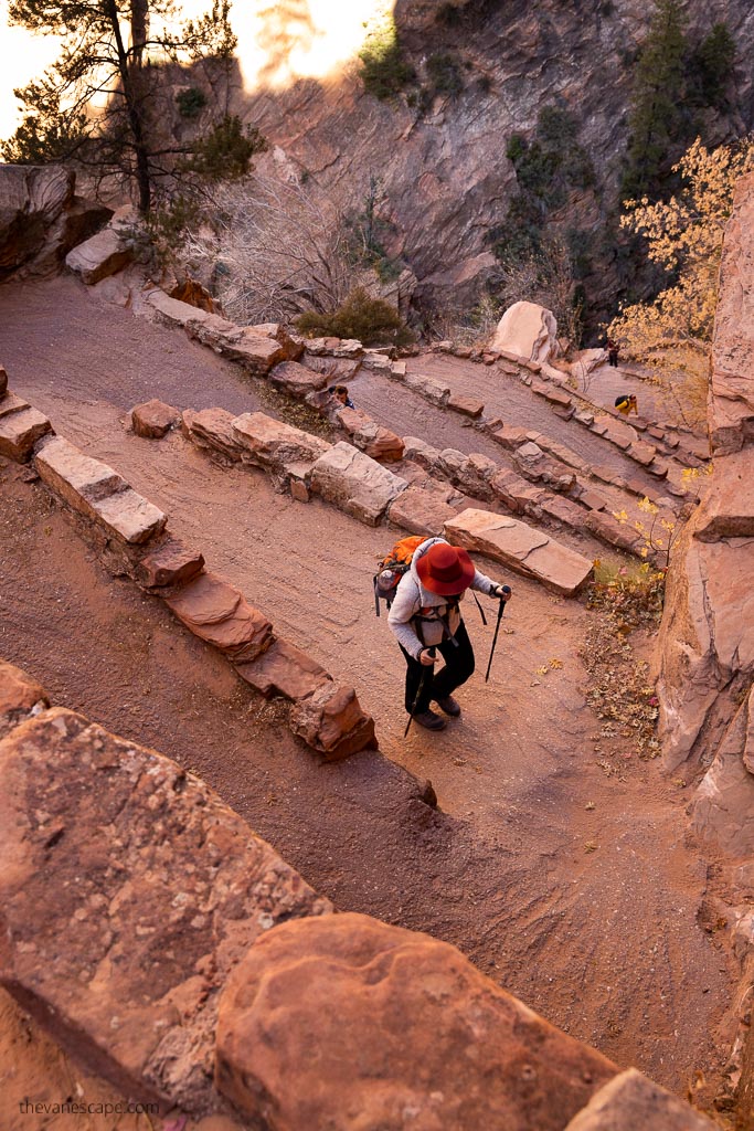 Agnes Stabinska, the author and co-founder of the Van Escape blog, climbs a serpentine path up the mountain on the trail to Angels Landing. She has trekking poles and a red sun hat.