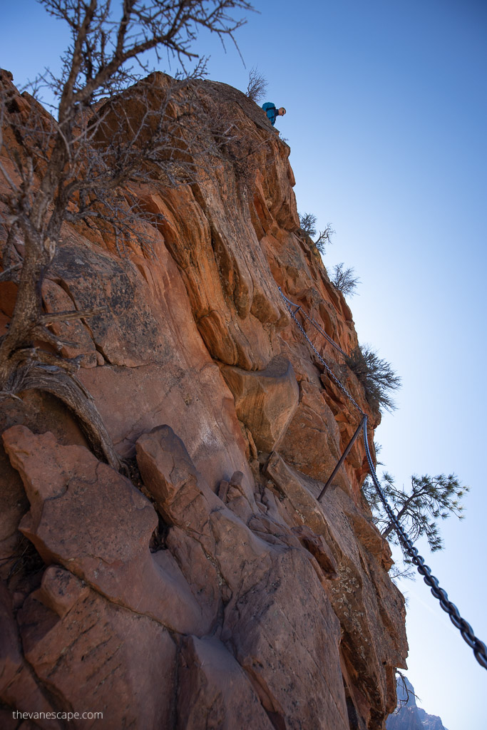 A section of chains leads to the top of Angels Landing, with a man looking down from the top.