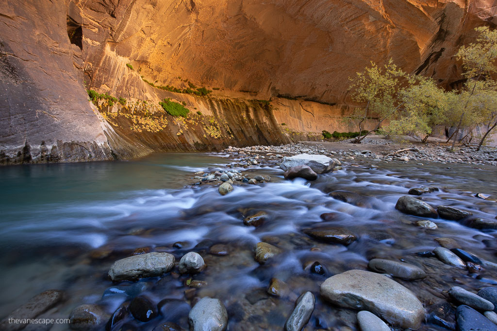 Wonderful light in zion national park during the Narrows Hike with water in the front and orange walls in the background.