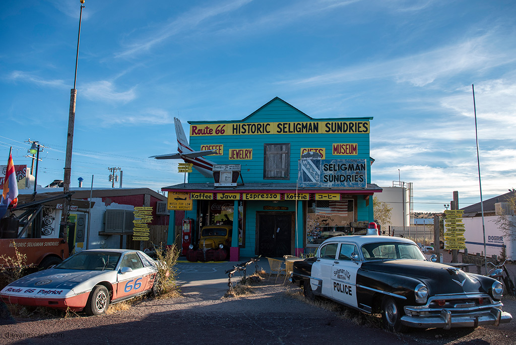 Historic Seligman buildings and old cars: police car and sport car at the front to Route 66 Historic Seligman Sundries blue wooden uildling.