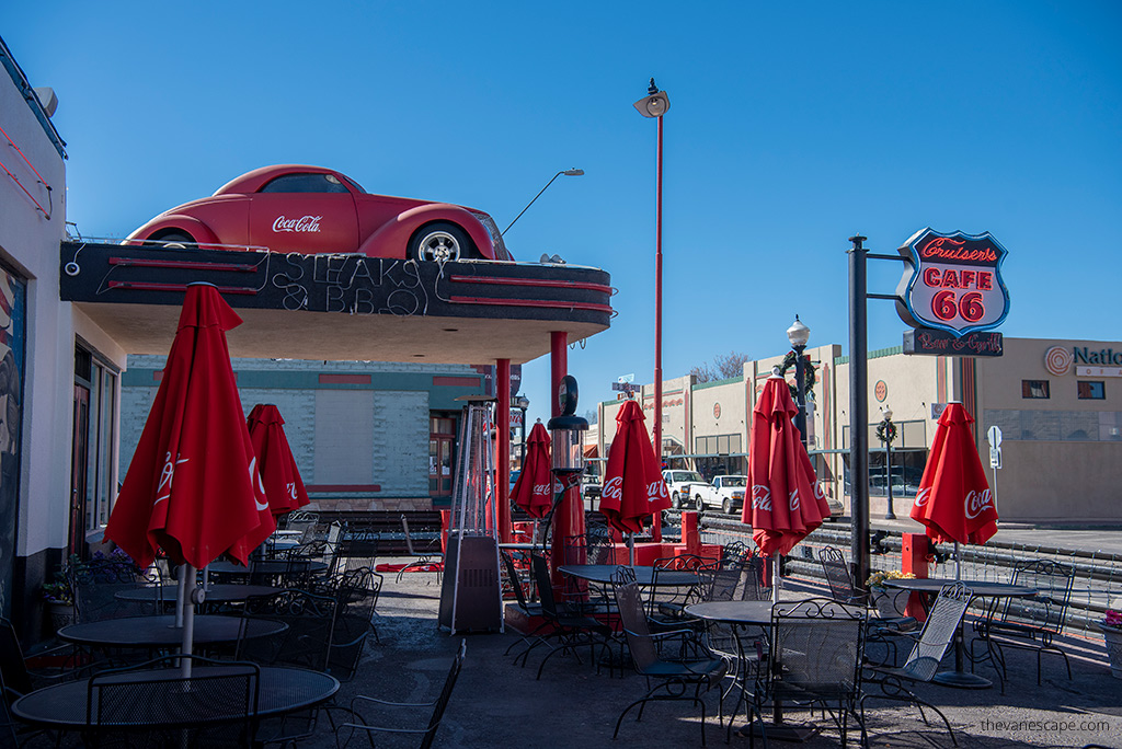 Williams  Arizona with old red car at the front of the entrance to the cafe 66. Metal round tables and red umbrellas with the inscription Coca-Cola in front of the entrance.