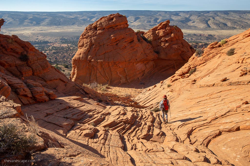 Agnes Stabinska, the author and co-owner of the Van Escape blog is hiking among orange and delicate rock formations at Coyote Buttes South Hike. She has trekking poles.
