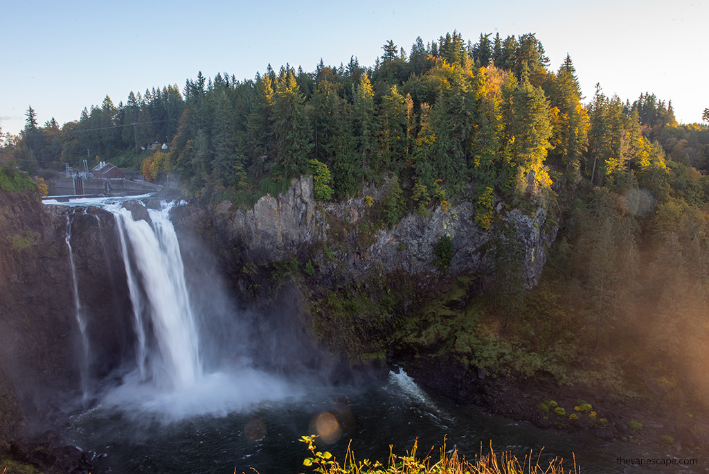 Sunset over Snoqualmie Falls: a cascade of water flows down the rocks, foam and fog fill the air.