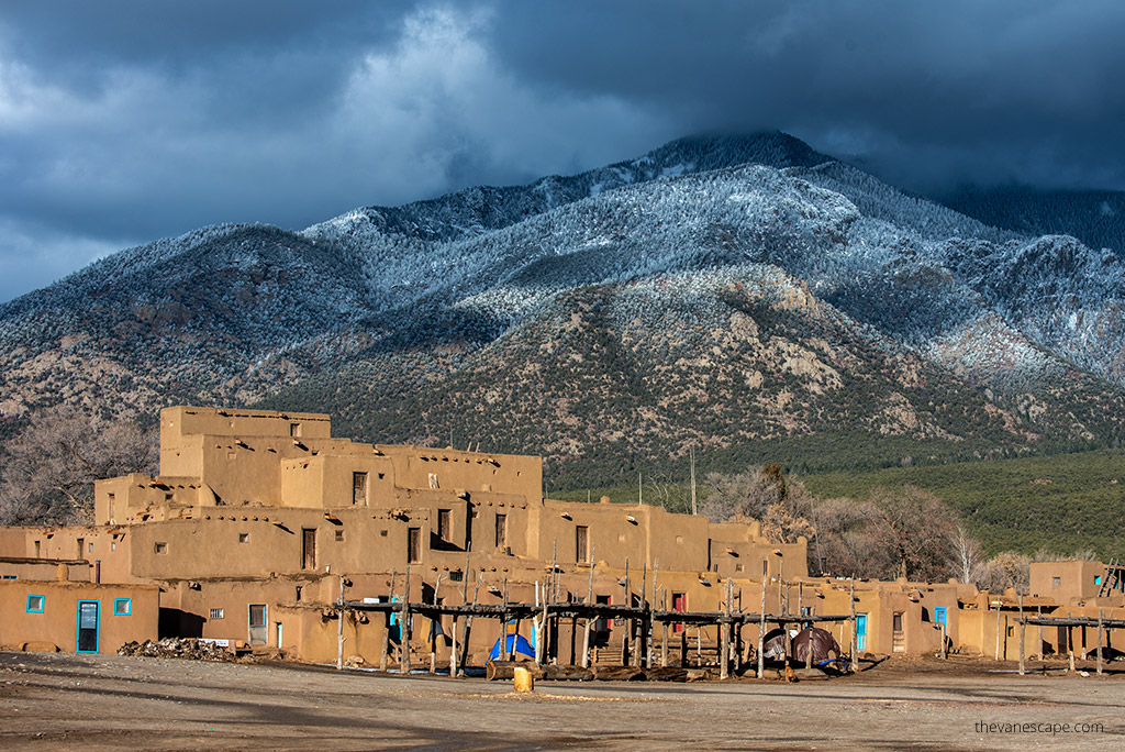 Taos Pueblo historic buildlings with the view of Sangre de Cristo Mountains covered by snow in the backdrop.