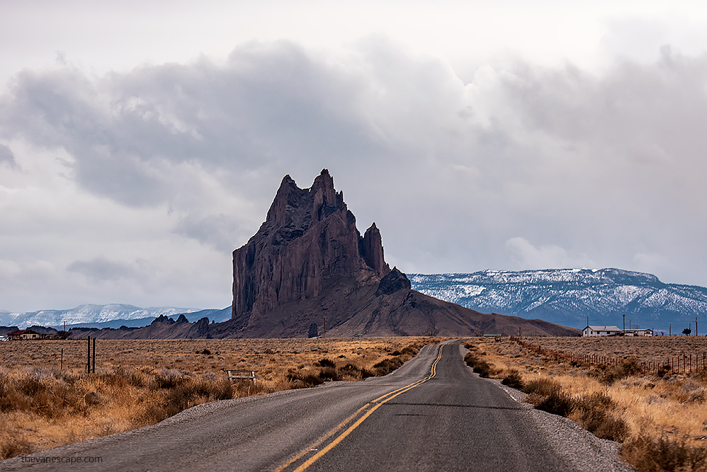 road to shiprock with the shiprock formation and mountains in the backdrop.