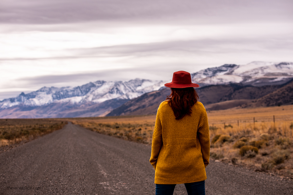 Agnes Stabinska, the author, in yellow sweater and red hat on the gravel road to Alvord Hot Springs with mountain view.