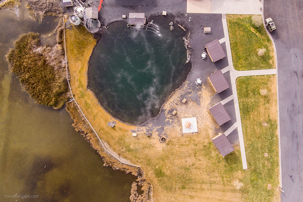 Drone view of Crystal Crane Hot Springs: large swimming pool with hot water and wooden huts along the pool that can be rented for the night.