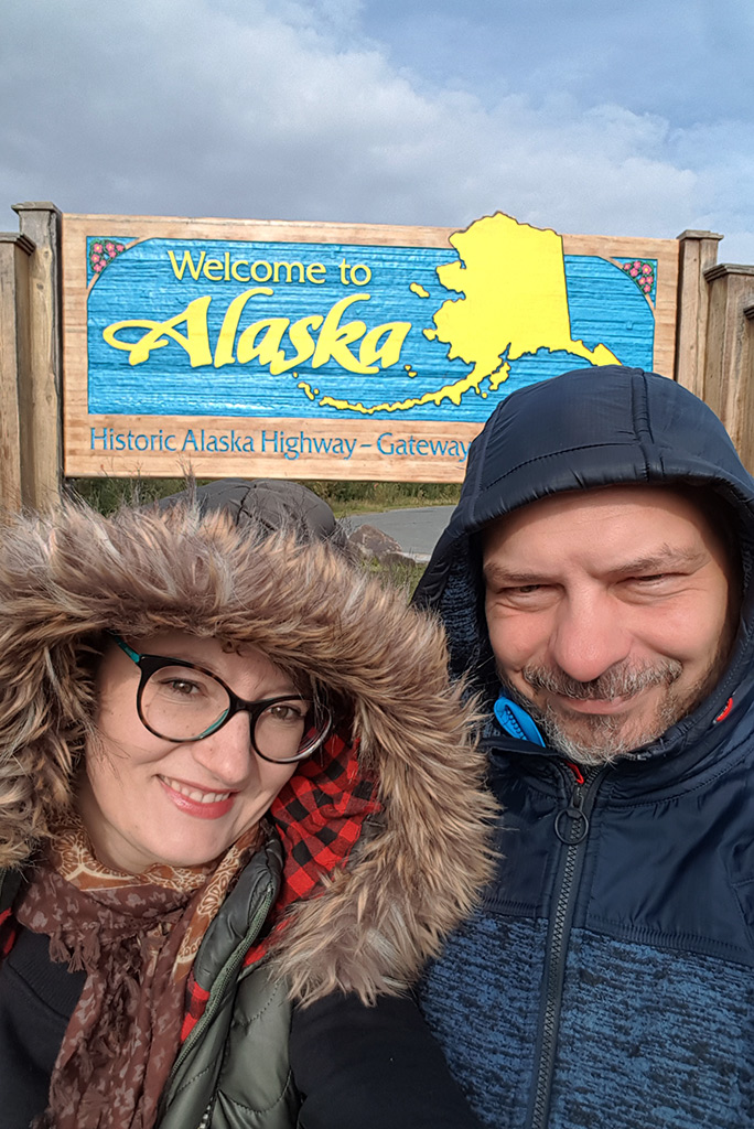 Agnes Stabinska, the author, and Chris Labanowski, her partner, owners of The Van Escape Blog, with the wooden sign welcome to Alaska.