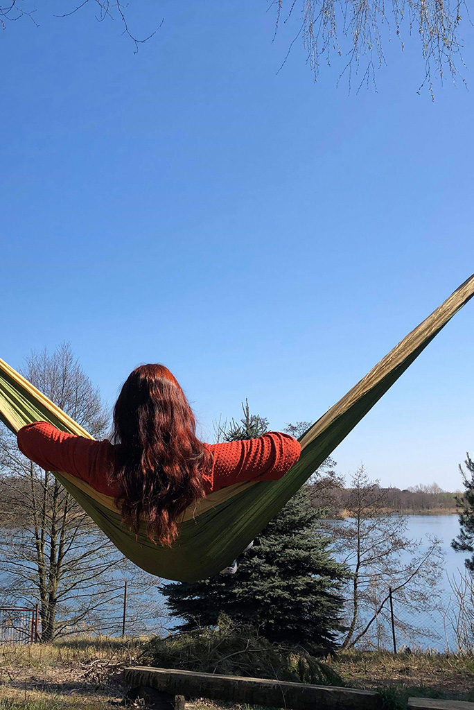 Agnes Stabinska, the author is relaxing in green camping hammock with the lake view.