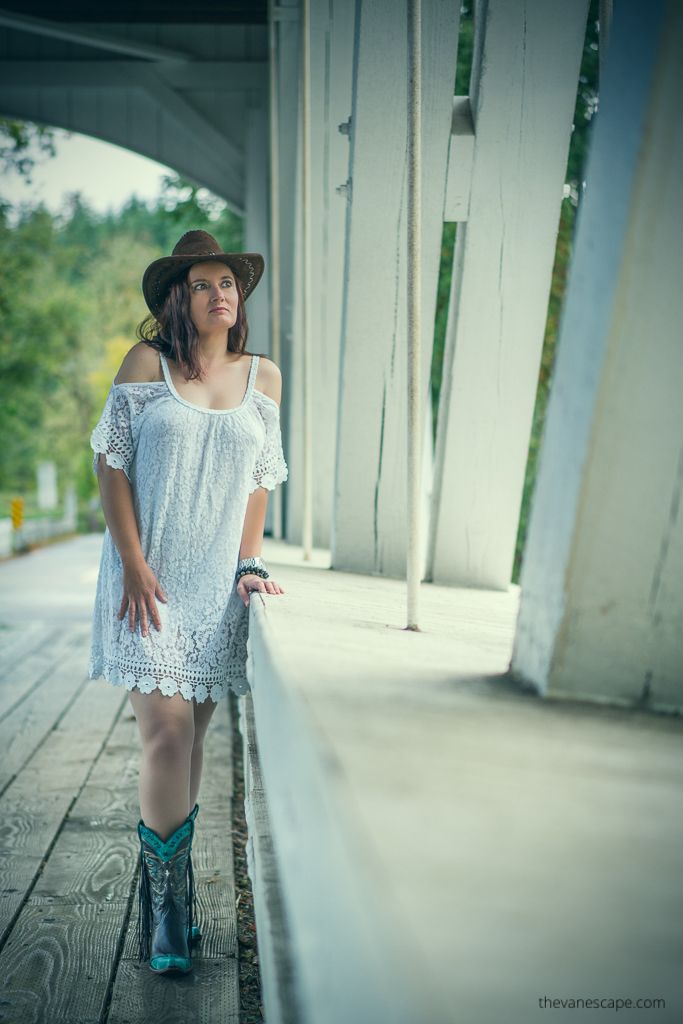 Agnes Stabinska, the author and co-founder of The Van Escape blod, is standing on the white Larwood Covered Bridge in Oregon. She is wearing white dress and cowboy boots and hat.