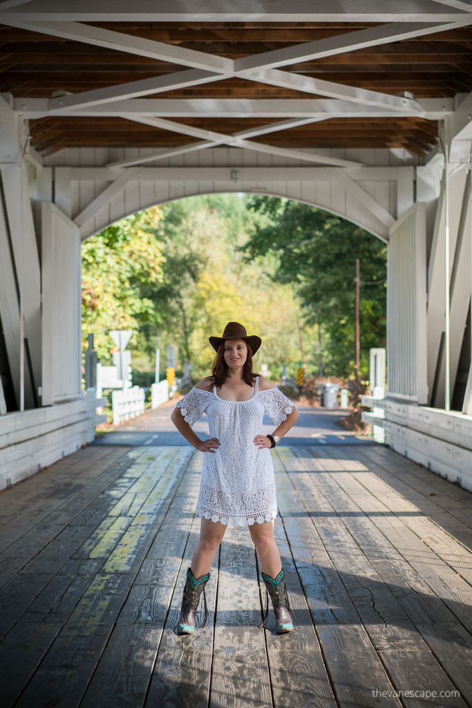 Agnes Stabinska, the author and co-founder of The Van Escape blod, is standing on the white Larwood Covered Bridge in Oregon. She is wearing white dress and cowboy boots and hat.