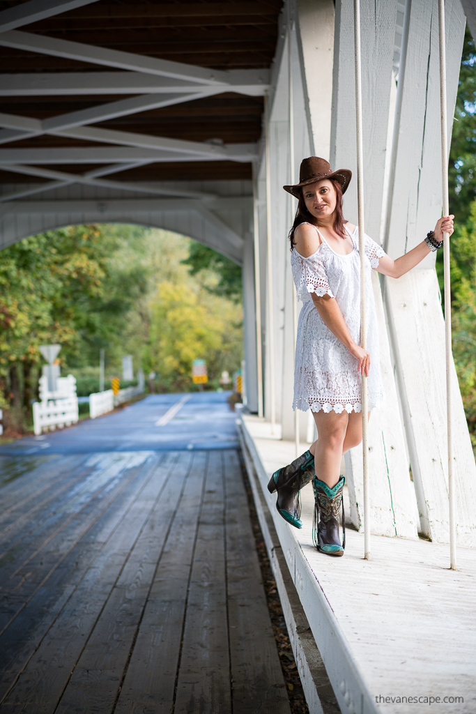 Agnes Stabinska, the author and co-founder of The Van Escape blod, is standing on the white Larwood Covered Bridge in Oregon. She is wearing white dress and cowboy boots and hat.