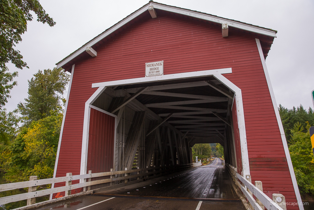 red wooden structure of Shimanek covered Bridge.