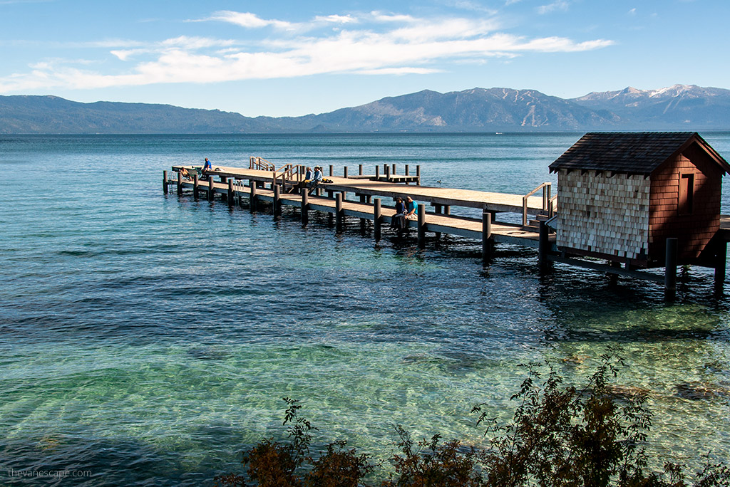 Lake Tahoe view: a wooden cottage and a wooden pier on the transparent surface of the lake in a beautiful mountain setting.