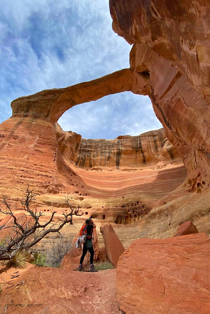 Agnes Stabinska, the author, in Rattlesnake Canyon, she stands under a huge, tall, orange-colored rock arch and takes a photo.