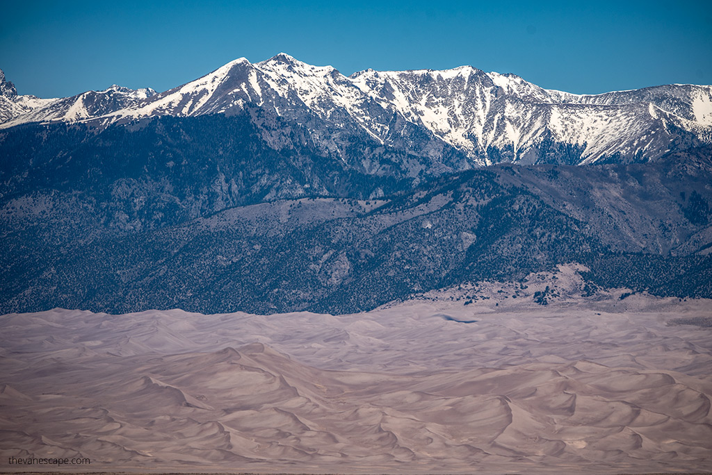 Great Sand Dunes National Park with mountains peaks covered by snow in the backdrop.