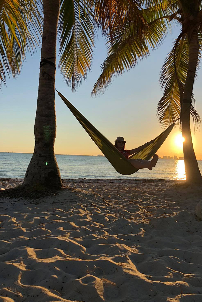 Agnes Stabinska, the author, on the beach during sunset is hanging in a the  Backpacking Hammock between palm trees. 