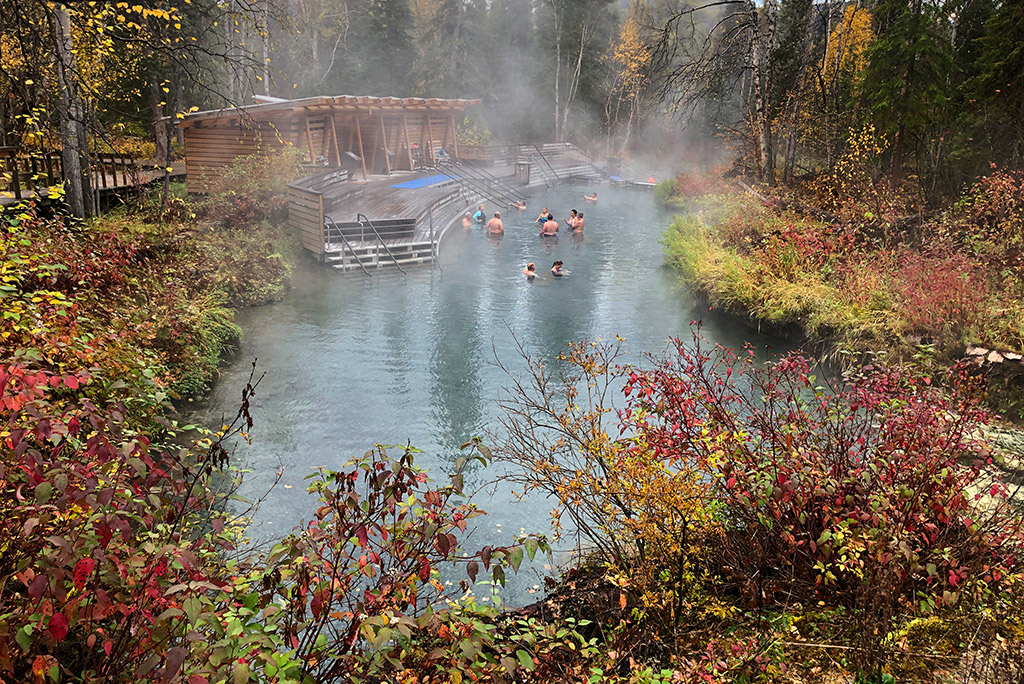 people soaking in Liard River Hot Springs in fall scenery with colorful leaves on trees. 