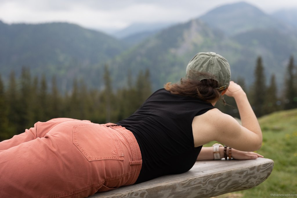 Agnes Stabinska, the author and co-founder of The Van Escape blog in KUHL KULTIVATR Women's Shorts is on the mountains. She lies on a wooden bench on the trail and admires the mountains.