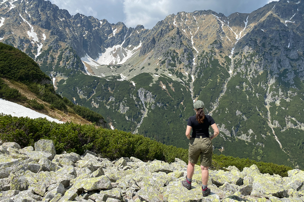 Agnes Stabinska, the author, in Kuhl shorts and hiking boots from our day hiking packing list, on the mountain trail with the scenic mountain view.