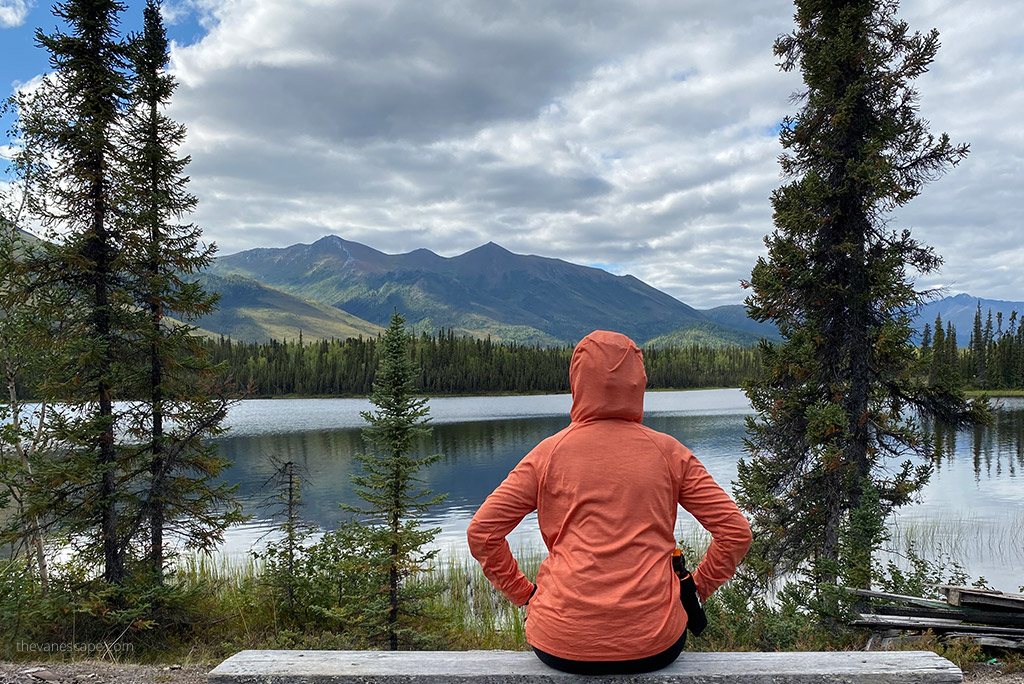 Agnes Stabinska, in orange hoodie is sitting on the bench with the lake view in Gates of Arctic National park in Alaska.