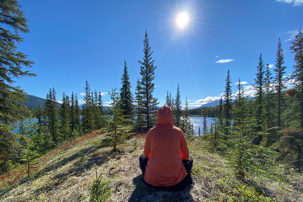 Agnes Stabinska, the author is sitting in orange KUHL ENGINEERED Women's Hoody among trees with the lake and mountain view.