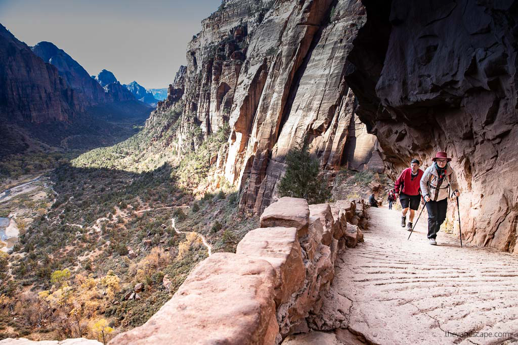 Agnes Stabinska, the author and co-founder of the Van Escape blog is hiking in Zion National Park, she is wearing red hat, flees jacket and she has trekking poles.