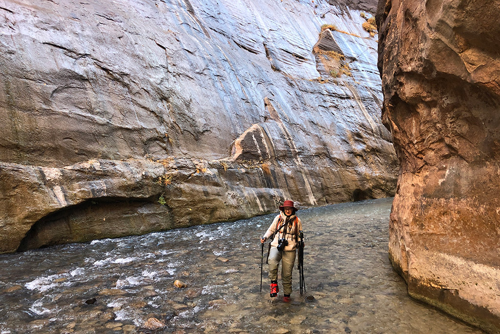 Agnes Stabinska, the author, is hiking in the water, in the Virgin River during the Narrows hike, she has water boots and [ants and trekking poles.
