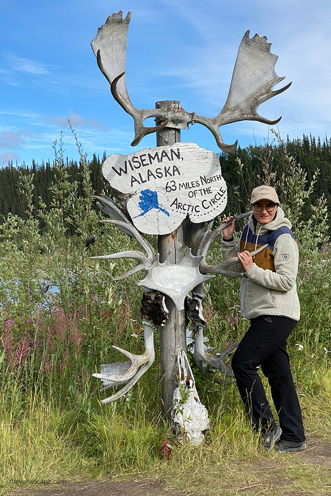 Agnes Stabinska, the author, in KUHL PRISM Hoody is standing next to the sign of Wiesman, ALaska with inscription: 63 miles north of the Arctic Circle.