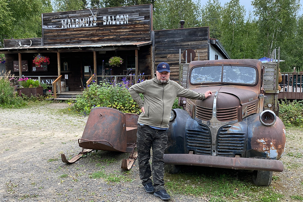 Chris Labanowski in KUHL SPEKTER Full Zip Hoody is standing next to old truck and wooden house with inscription: Malemute Saloon, it's on Alaska.