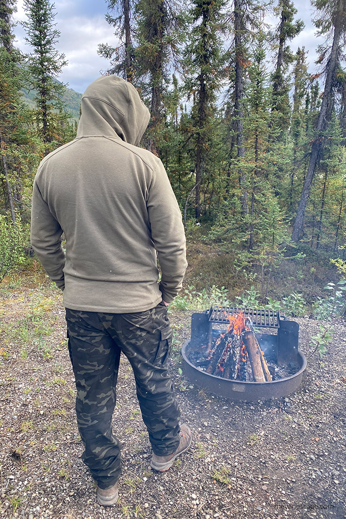 Chris Labanowski in hoodie by Kuhl on Alaska camping, next to campfire.