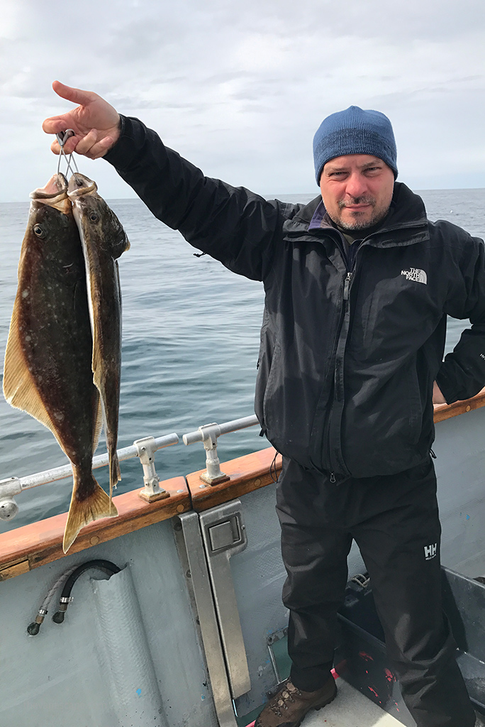 Chris with halibut on a boat during halibut fishing tour in Homer on a Gulf of Alaska: