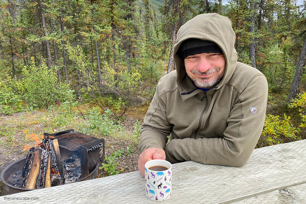 Chris Labanowski is sitting next to campfire and drinking a coffe, he is wearing KUHL SPEKTER Full Zip Hoody.