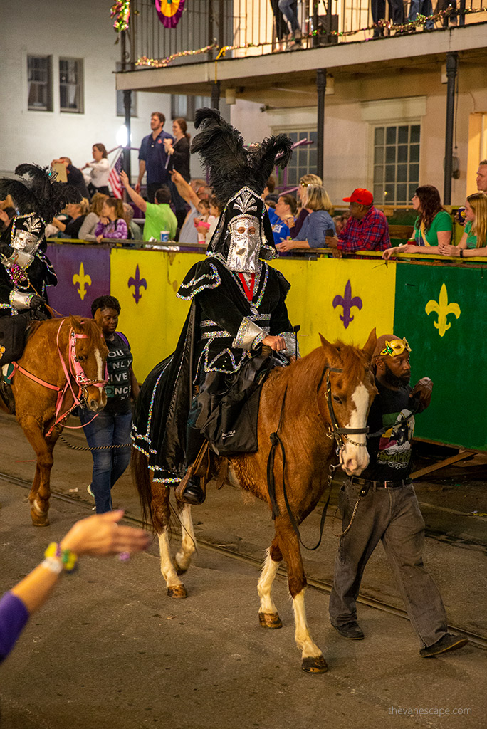 Men with a face mask and black costumes are on the horse on New Orleans streets.