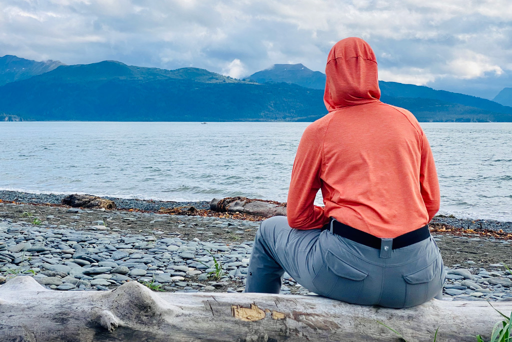 Agnes Stabinska, the author co-owner of The Van Escape blog is sitting on a tree trunk in grey KUHL FREEFLEX ROLL-UP Pants. She is looking at the sea and mountains. 