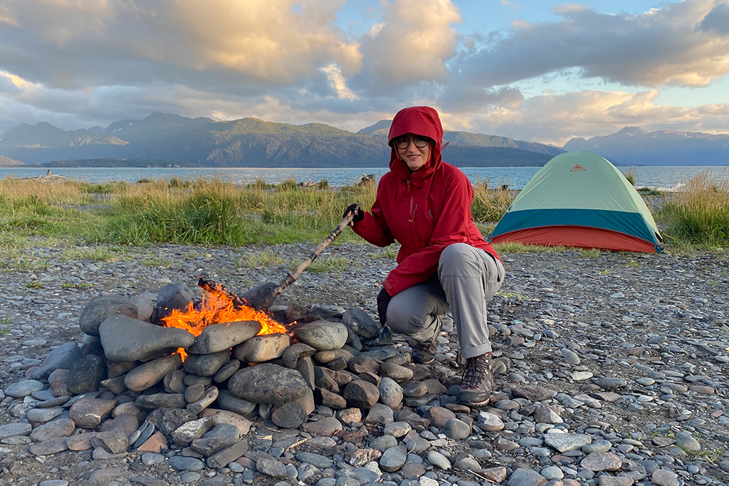 Agnes Stabinska, the author, next to campfire on camping, with a tent and the sea in the backdrop.