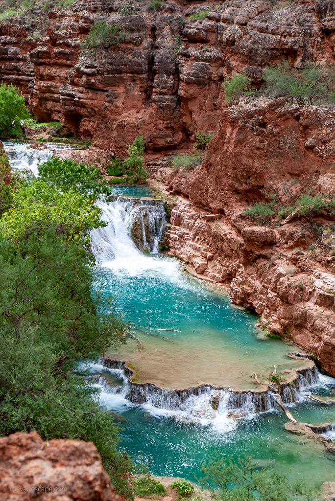 Stunning blue water of Havasu Falls flowing down high orange rocks, greenery all around.