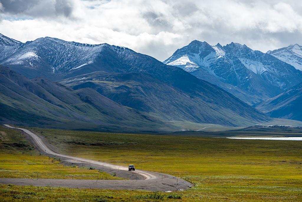 car on a gravel road with alaska mountains in the backdrop.