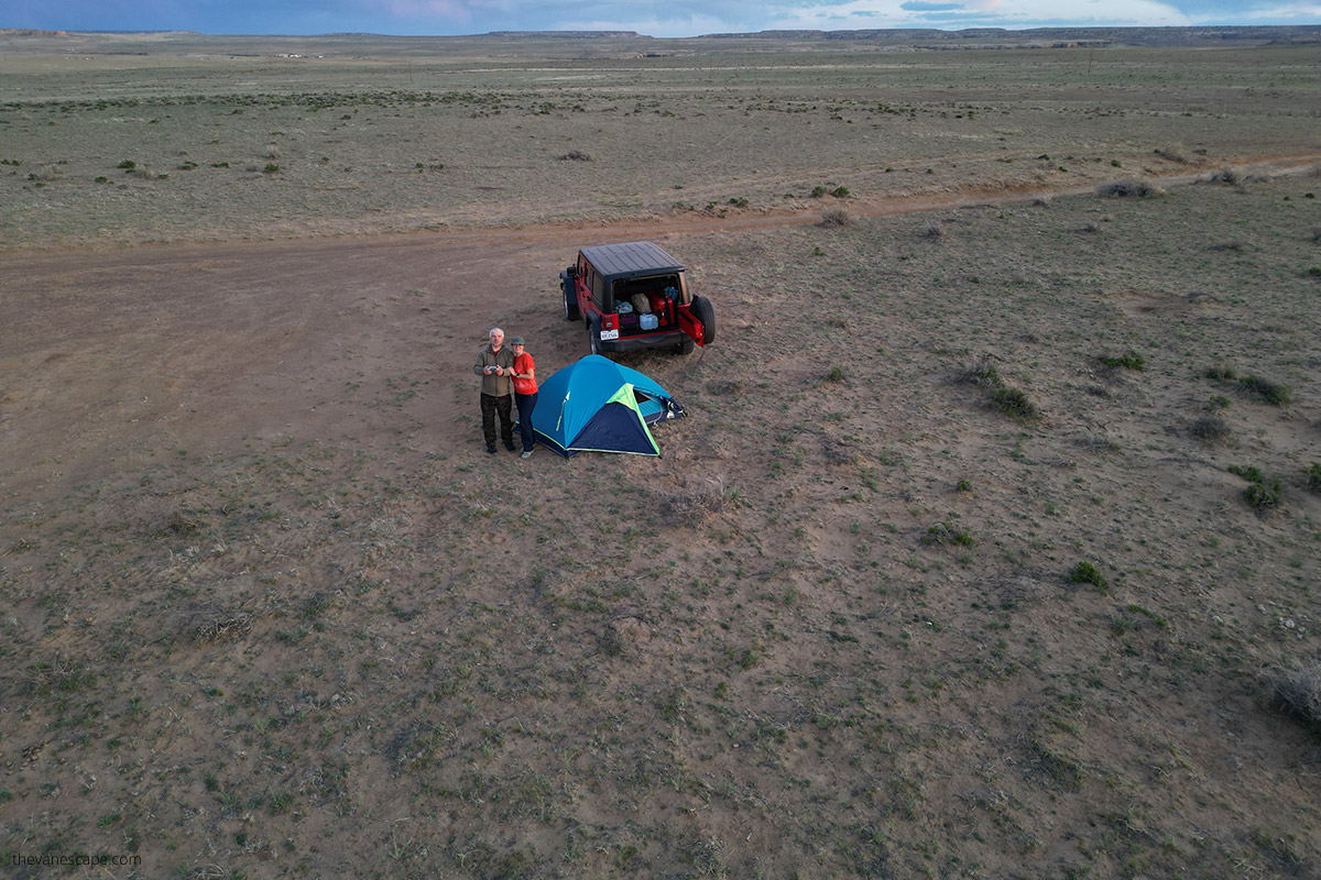 Agnes Stabinska and Chris Labanowski, the owners of the Van Escape blog, are standing next to tent and red jeep and taking a pictures from a bird perspective with drone.