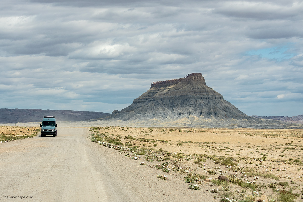 van driving gravel Factory Butte Road with the background of huge and colorful butte