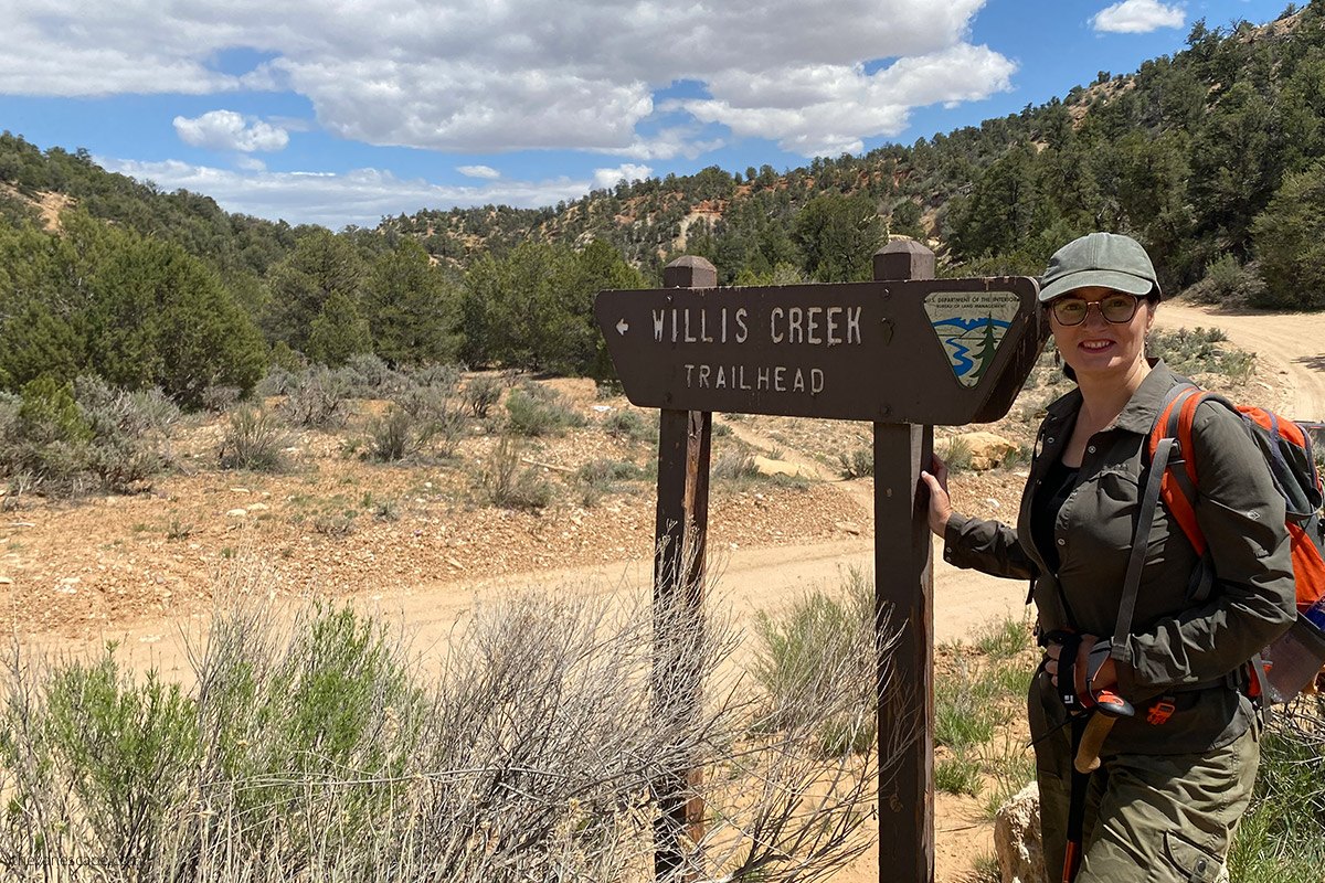 Agnes with the wooden sign which is pointed the beginning of the Willis Creek Trailhead