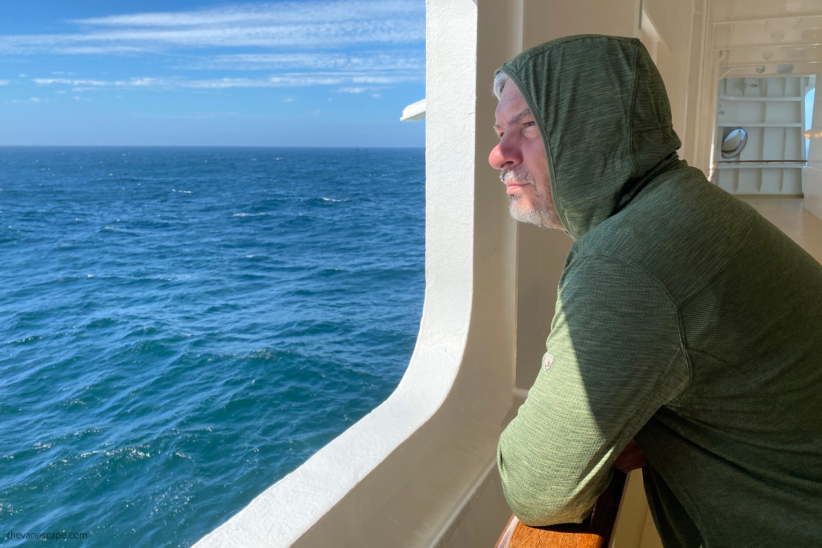 Chris looking for the sea from ship window wearing green Kuhl sun protection t-shirt with a hood