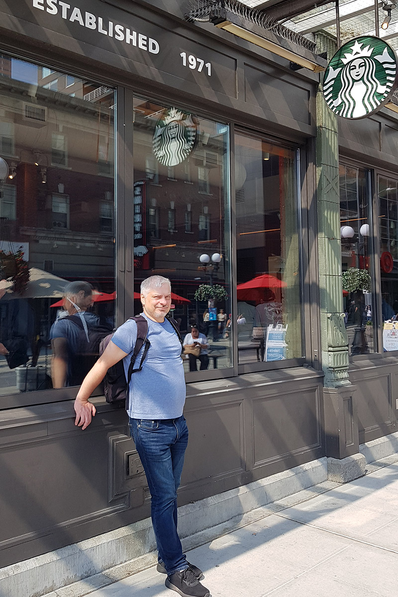 Chris Labanoski, co-founder of the Van Escape blog is standing at the fron of Sturbucks in Seattle with inscription: Established in 1971 on the wall.