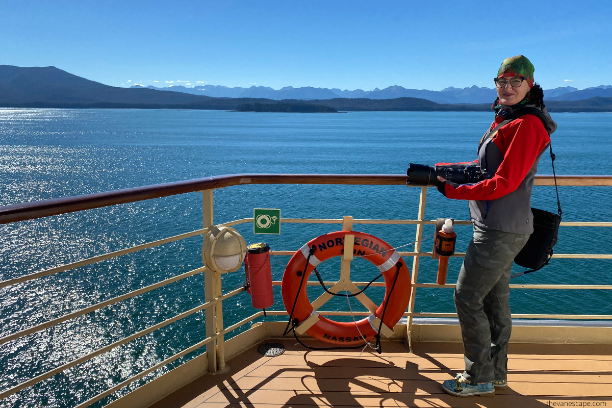 Agnes with her camera on Norwegian Sun ship during sunny day on Alaska cruise with mountains in the backdrop