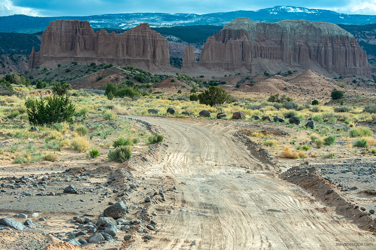 dirty road in Cathedral Valley with massive rock formations and snowy mountains in the backdrop