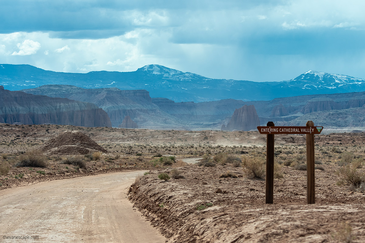 wooden sign: entering cathedral valley with mountains in the backdrop